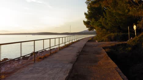 Dolly-in-of-concrete-promenade,-rocky-shore-and-calm-sea,-golden-hour