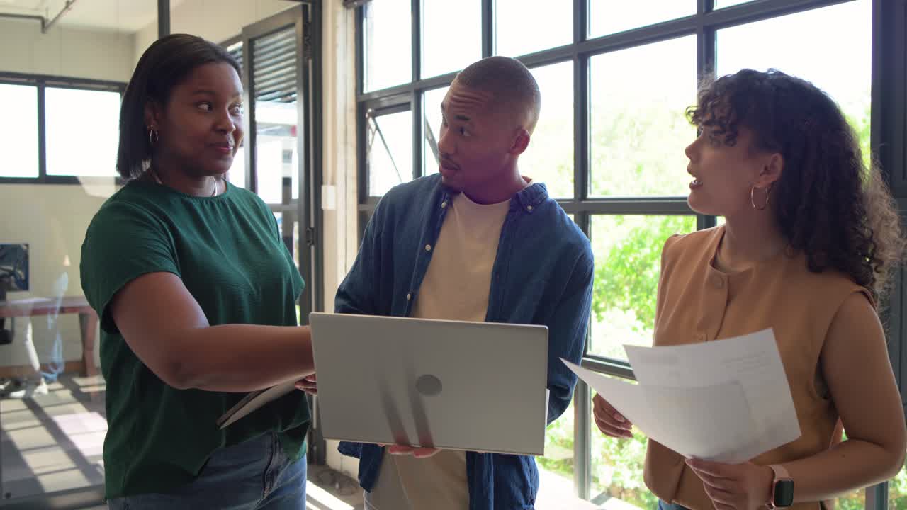 African American team reviewing papers and tablet by grid window after man opening laptop, deciding
