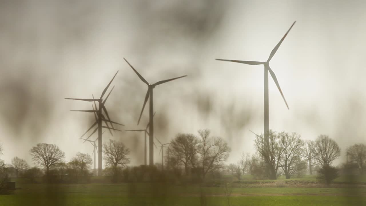 시골 환경에 있는 풍력 발전소의 평화로운 흑백 묘사, 네 개의 움직이는 세  ⁇ 의  ⁇  풍력 터빈이 구름이 가득한 하늘 아래의 나무와  ⁇  사이에, 안개 같은 꿈 같은 오라와 함께