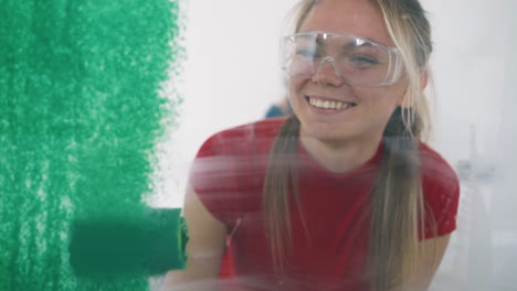 girl-in-goggles-paints-wall-with-green-using-roller-in-room