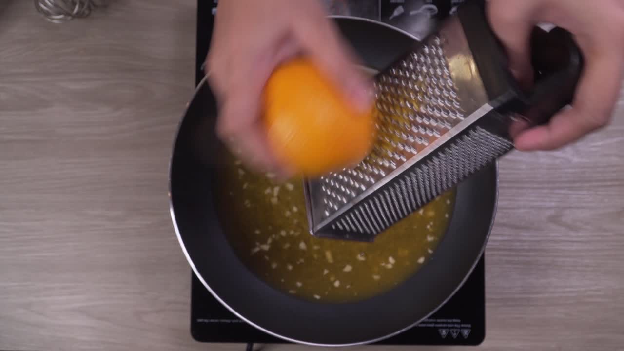 Close up on female hands grating orange zest into frying pan