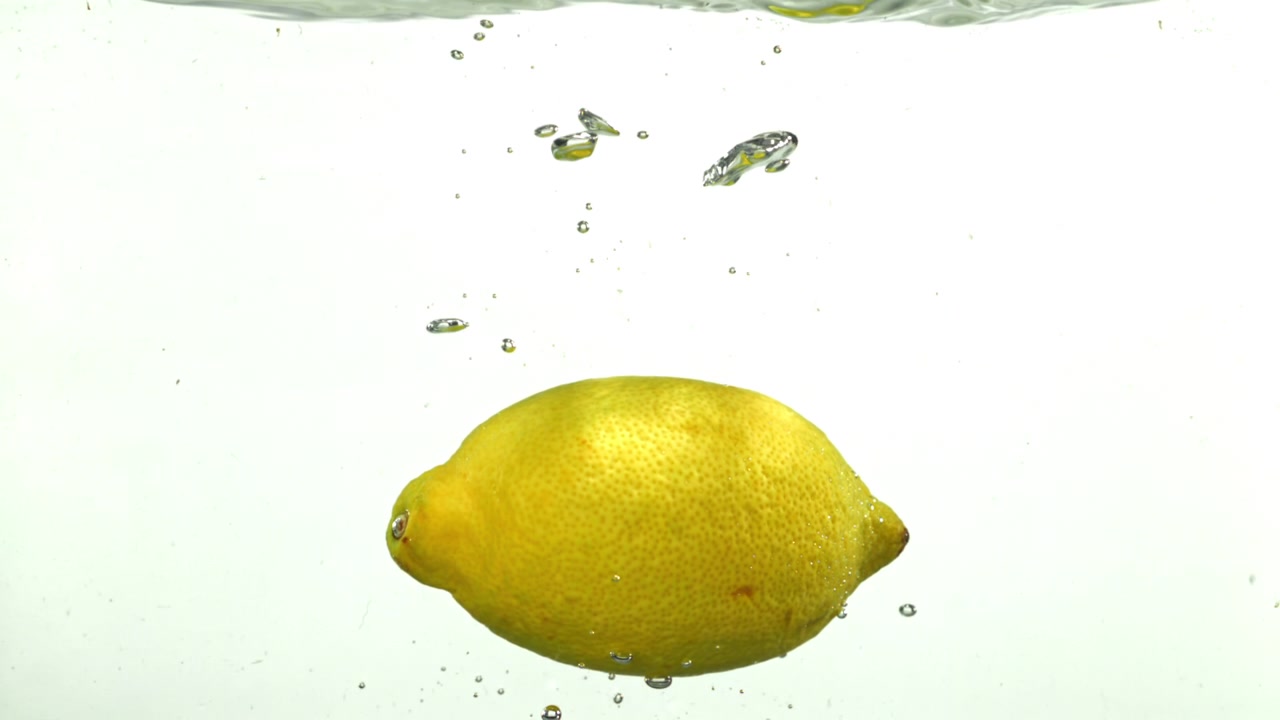 Limone giallo che galleggia in acqua limpida con bolle.
