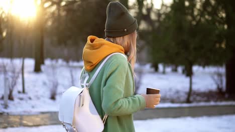 mujer caminando con bebida caliente por el parque de la ciudad de invierno, disfrute del clima, vista lateral