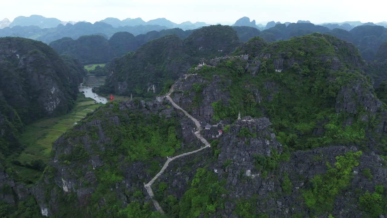 Aerial pan right revealing stone stairways, viewpoint platforms and rugged cliffs along mountain in Ninh Binh