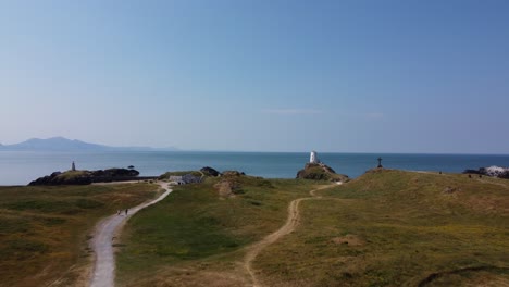 aerial view following ynys llanddwyn coastal walking trail towards goleudy tŵr mawr stone lighthouse, anglesey