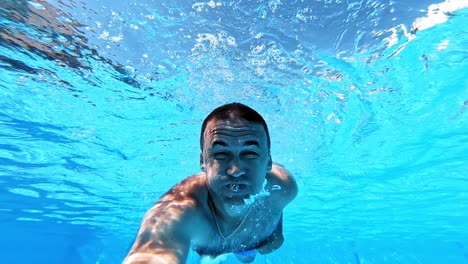 man smiling on camera underwater in the pool. happy man dives under the blue clear water and swimming inside the swimming pool in summer.