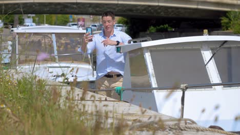 a-young-Caucasian-man-on-his-small-boat-making-a-video-call-with-his-smartphone