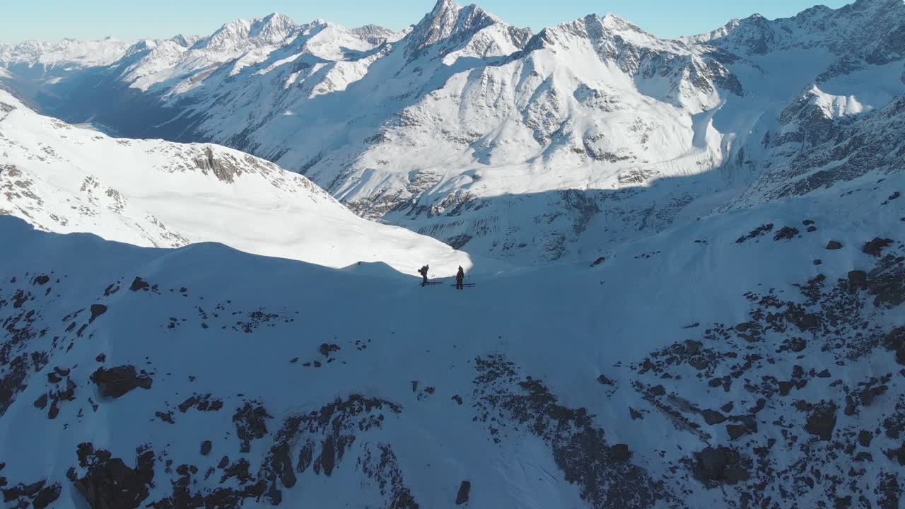 vista aérea sobre montañeros, con esquís en la cima de una montaña, soleado, día de invierno en los alpes - retroceder, tiro con drones