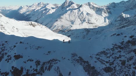 aerial view over mountaineers, with skis on top of a mountain ridge, sunny, winter day in the alps - pull back, drone shot