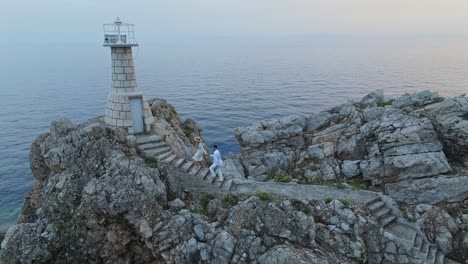 Isla-De-Kalamota,-Mar-Adriático,-Croacia---Una-Pareja-Dirigiéndose-Al-Faro-Para-Admirar-La-Puesta-De-Sol---Toma-Aérea-De-Retroceso