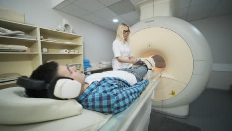 woman doctor makes knee-joint mri scanning. young man patient on automatic table enters into a closed-type mri machine using noise isolation headphones. modern equipment, coil on the patient's knee