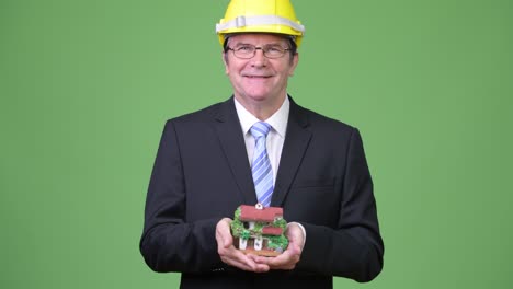 Senior handsome businessman as engineer holding house figurine
