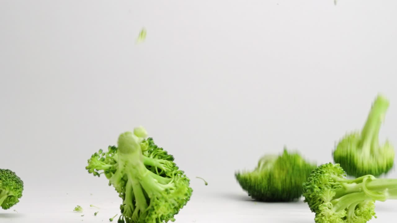 Pieces of broccoli falling and bouncing onto white studio backdrop in slow motion 4k