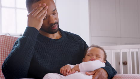 Nuevo-Padre-Estresado-Sentado-En-Una-Silla-Sosteniendo-A-Una-Niña-Dormida-En-La-Guardería-En-Casa