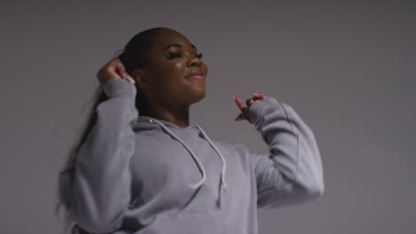 studio portrait shot of young woman wearing hoodie dancing with low key lighting against grey background 15