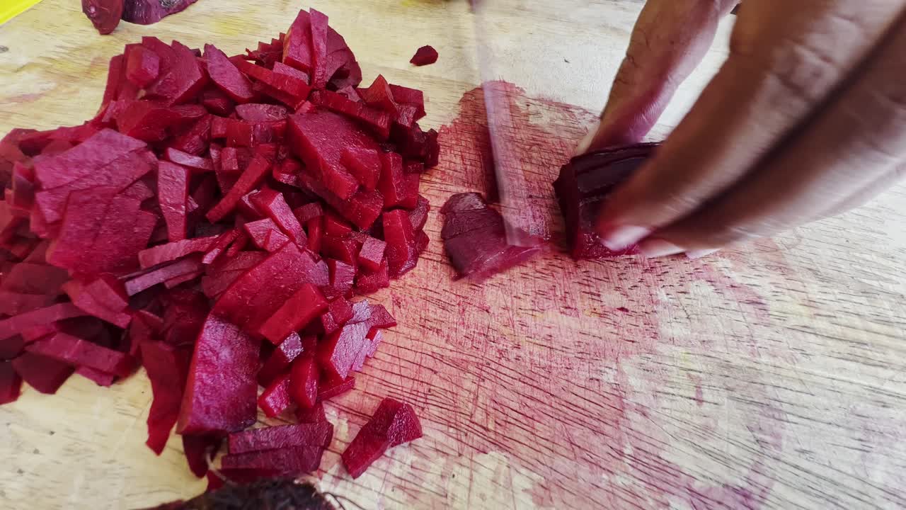 Close-up. Women's hands cut red peeled beet on a wooden cutting board with a kitchen knife into thin, long slices