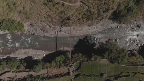 metal-wire-suspension-bridge-spanning-across-a-rocky-mountain-river-in-Kabayan-Benguet-Philippines-bird's-eye-view-top-down-wide-angle-aerial