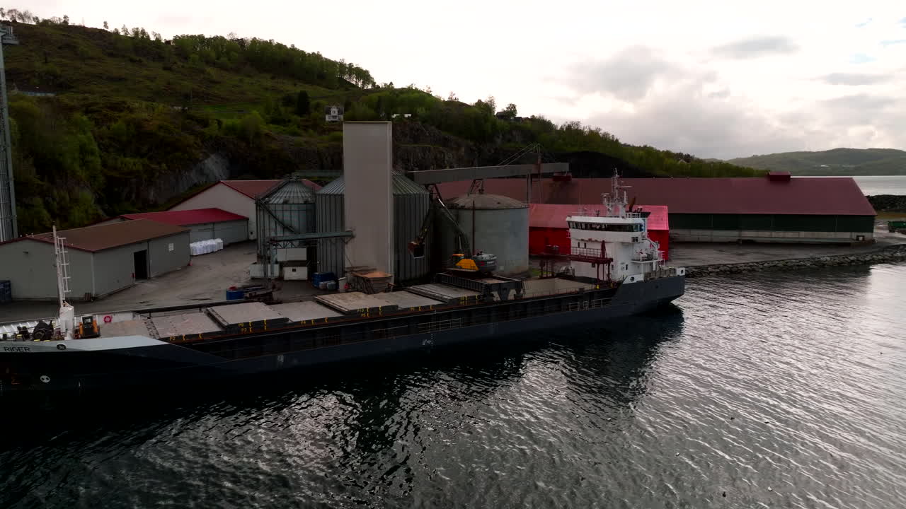 Cargo ship unloading soy at animal feed factory, industrial process, silos, and logistics in food production supply chain. Norway. Aerial drone