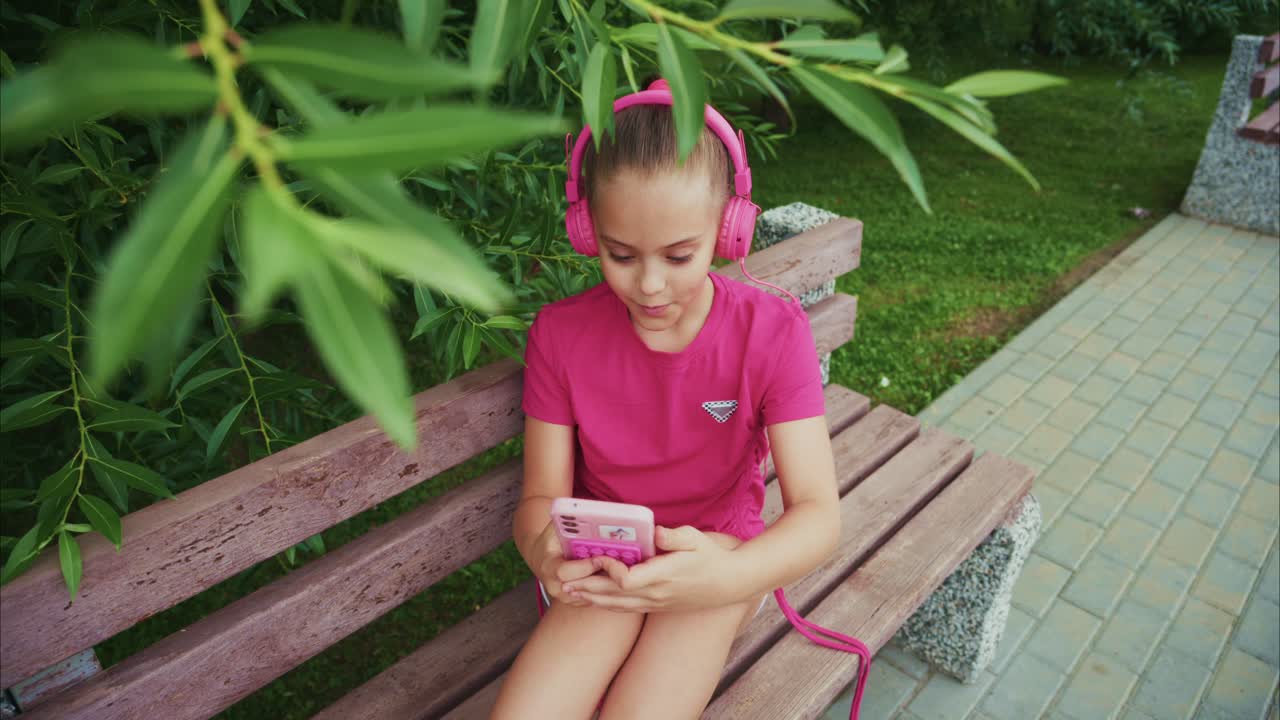 A Young Girl Enjoys Her Favorite Music while Relaxing on a Park Bench Surrounded by Lush Greenery and Natural Beauty