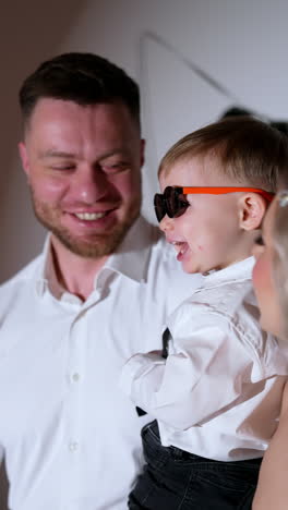 happy smiling caucasian man holds a lovely little baby boy wearing sunglasses. father and son together. studio footage. vertical video.