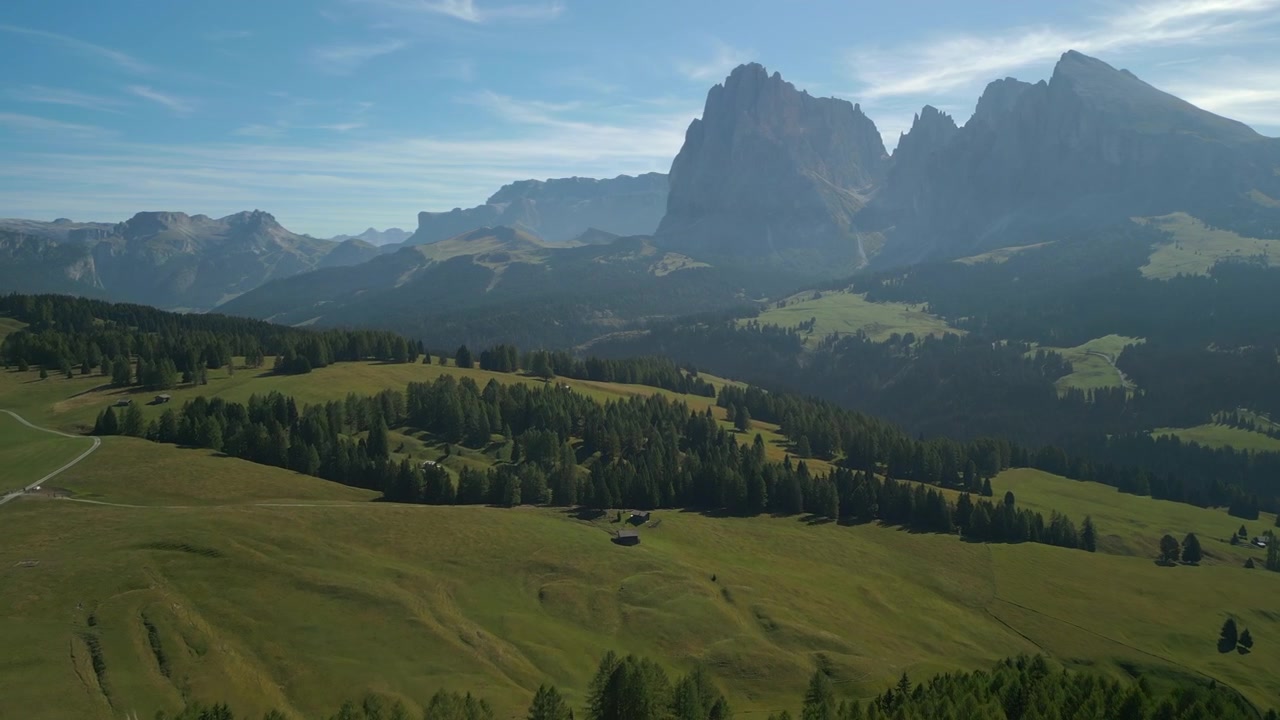 Pini e scogliera che si aprono su una vasta valle con cime dolomitiche velate. Ripresa aerea veloce, cinematografica e dal basso in una soleggiata giornata estiva.