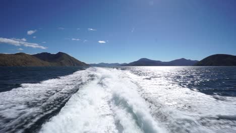 parte trasera de las olas del barco con cielo azul y montañas en segundo plano.