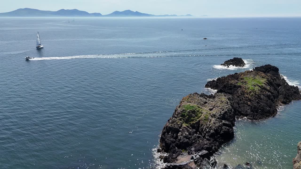 Aerial drone footage showcases solitary beacon perched on rugged, rocky coastline in England, UK, by vast seascape during sunny day