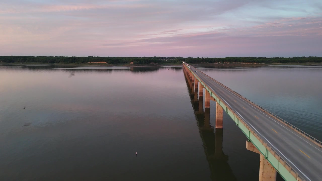 Riprese drone del Ponte lungo un miglio al lago Saylorville, Iowa, al crepuscolo, con la lunga passerella di legno che si estende su acqua calma riflettendo il cielo serale rosa e viola.