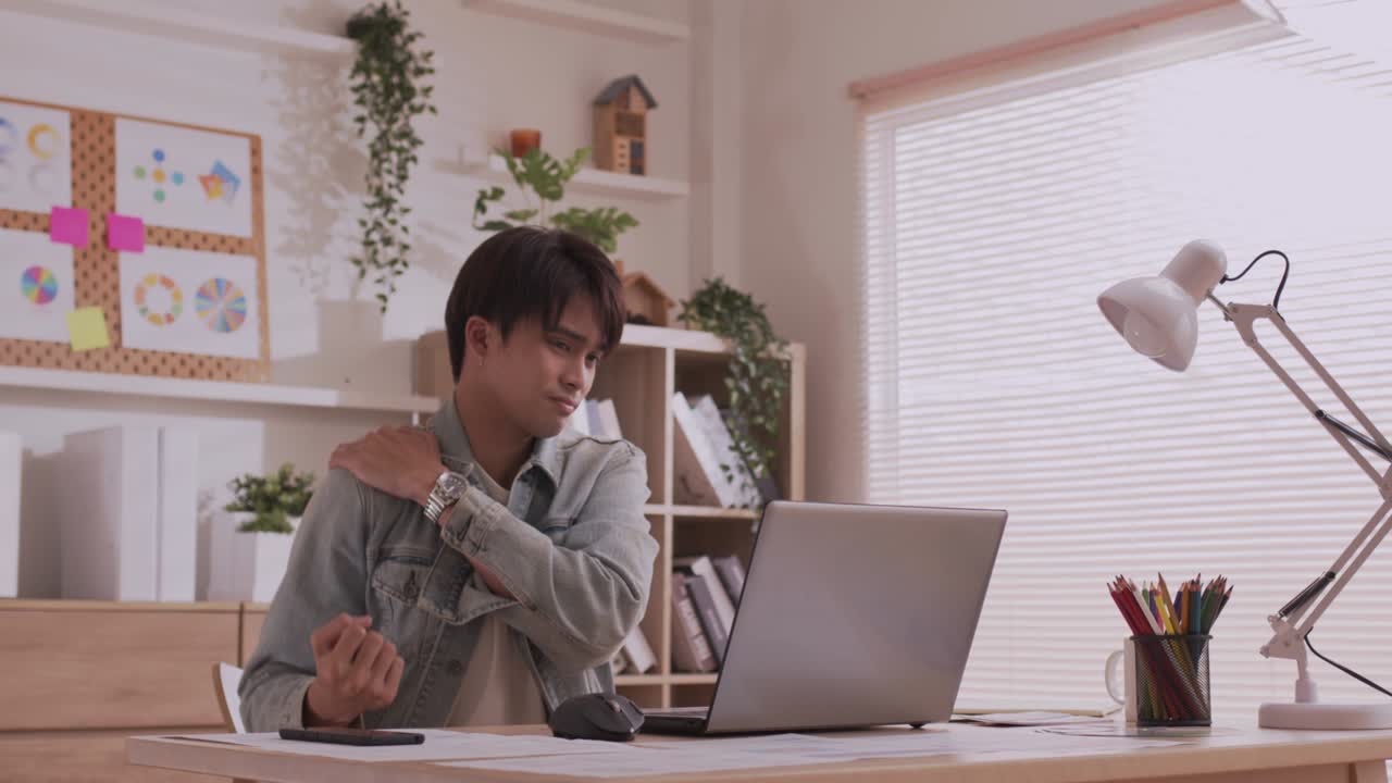 노트북을 들고 책상에 앉아서 온라인에서 연구를 한 후, 아시아의 사업가가 휴식을 취하기 위해 팔을 펴고 있다.