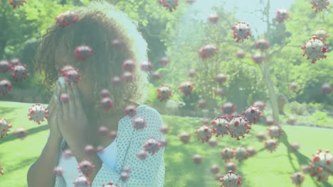 animation of macro covid-19 cells floating over biracial woman sneezing into a tissue