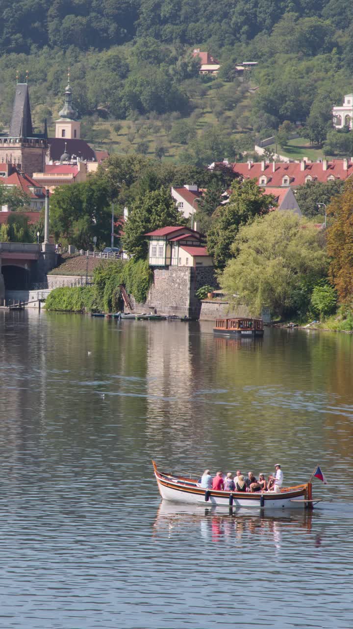 Piccola barca passeggeri si muove tranquillamente lungo il fiume Moldava con lo scenografico paesaggio urbano di Praga sullo sfondo