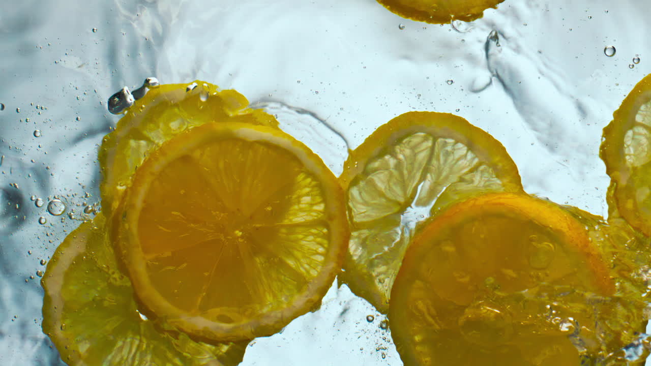 Sliced sour lemon falling water making splashes in super slow motion close up.