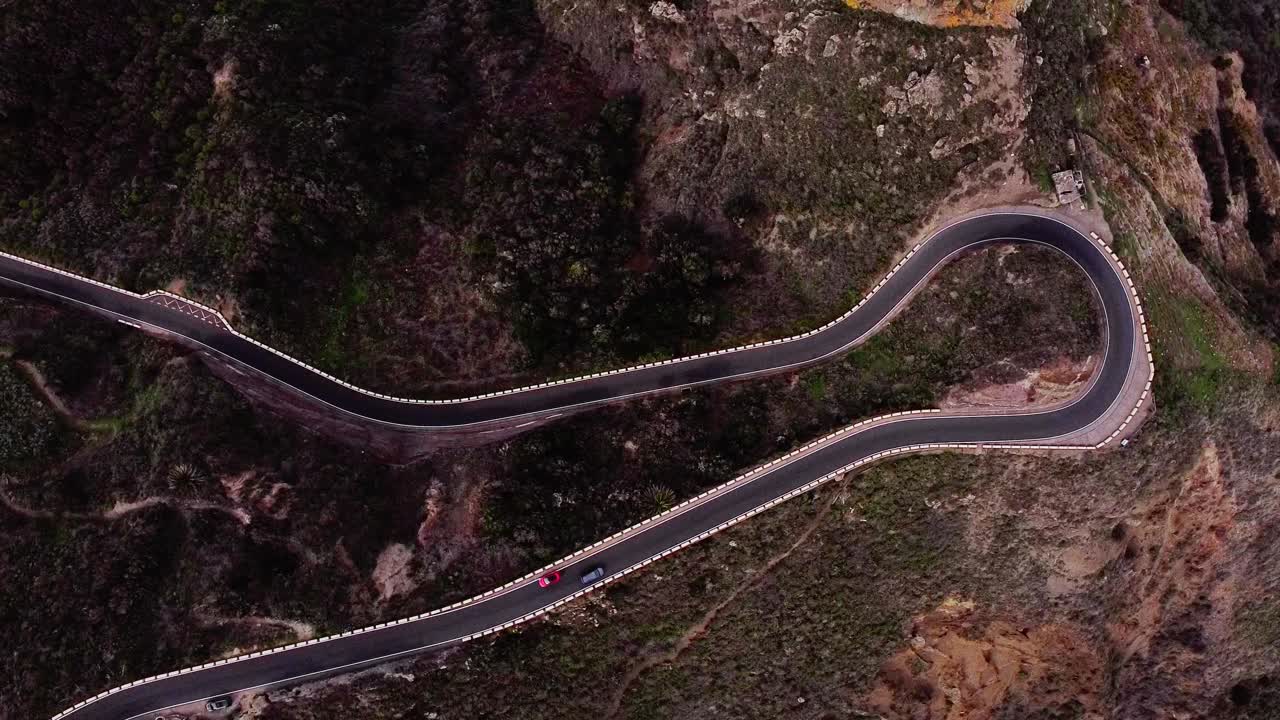 carretera serpenteante sinuosa con coches que conducen durante la hora de la noche en terreno rocoso, aire arriba abajo, tenerife