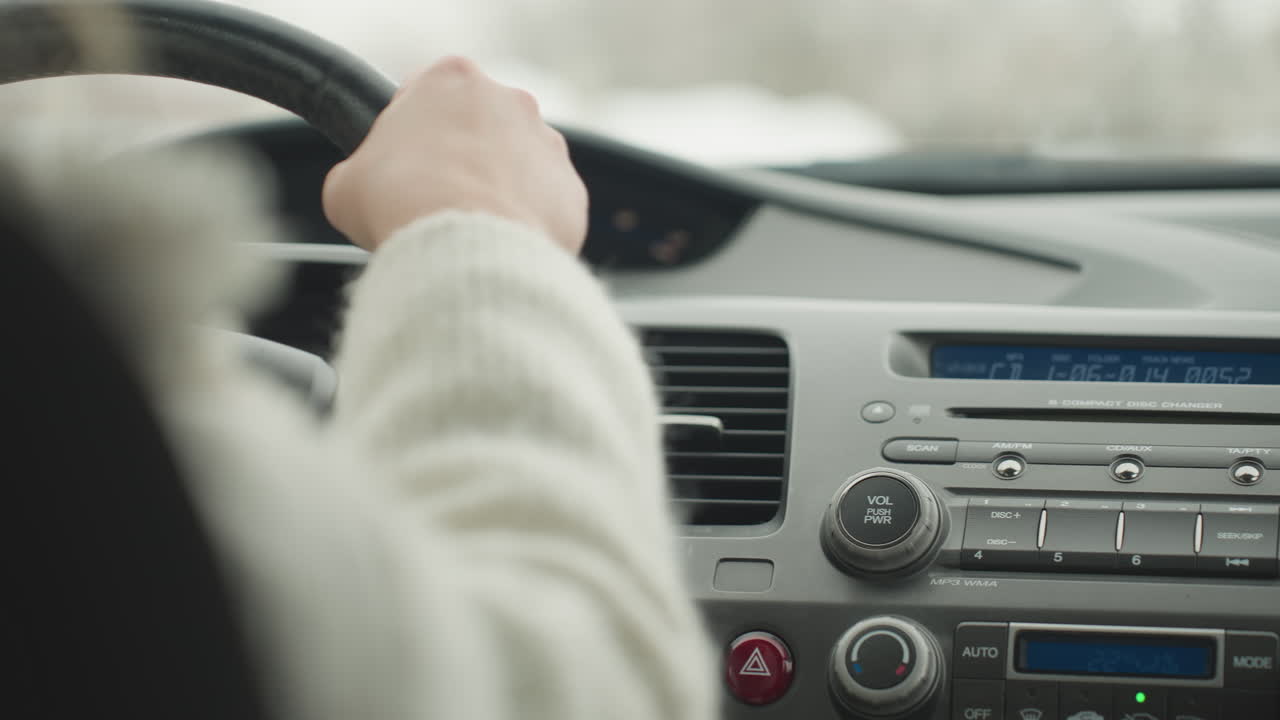 Close up rear view of lady driving car with dashboard stereo, steering wheel, and control buttons clearly visible while outside background remains blurred
