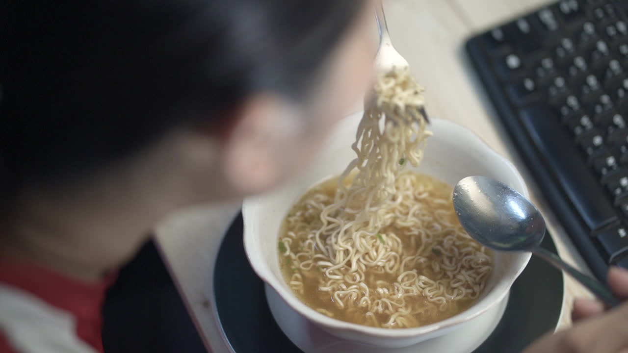 woman hand  eating hot instant noodles in food container on the desk