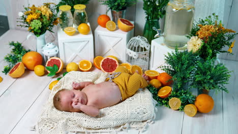 cute newborn in yellow pants only lies on the knitted pillow. baby's studio video in the surrounding of citruses and green plants.