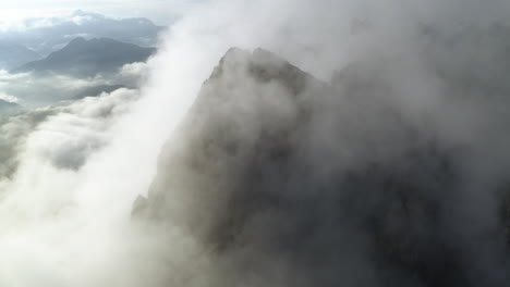 aerial view around a steep, foggy mountain peak, sunny day in dolomites, italy