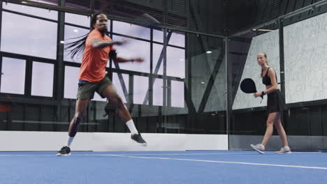 man and woman playing padel tennis on indoor court, enjoying competitive match
