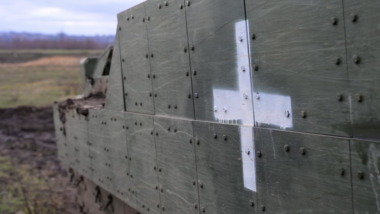 A detailed shot of the bolted appliqué armor on a US-made M2 Bradley in Ukraine. The stark white cross indicates its use as a frontline armored ambulance or MEDEVAC vehicle