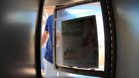 POV-from-inside-of-a-newspaper-vending-machine,-a-man-wearing-a-mask-and-earbuds-opens-the-container-placing-a-magazine-inside