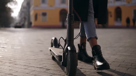 Cerca-De-Las-Piernas-De-Una-Joven-Conductora-De-Scooter-Caminando-Con-Su-Transporte-Ecológico,-Scooter-Eléctrico