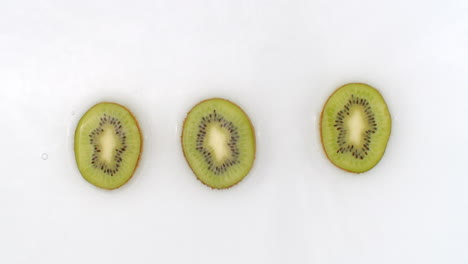 Three-kiwi-lie-on-white-in-background-in-slow-motion-falling-water-splashes.