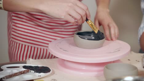 woman painting a ceramic bowl on a pottery wheel