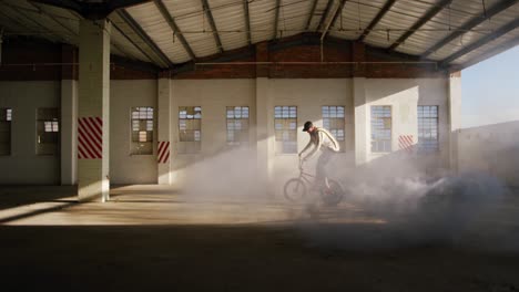 jinete de bmx en un almacén vacío usando una granada de humo