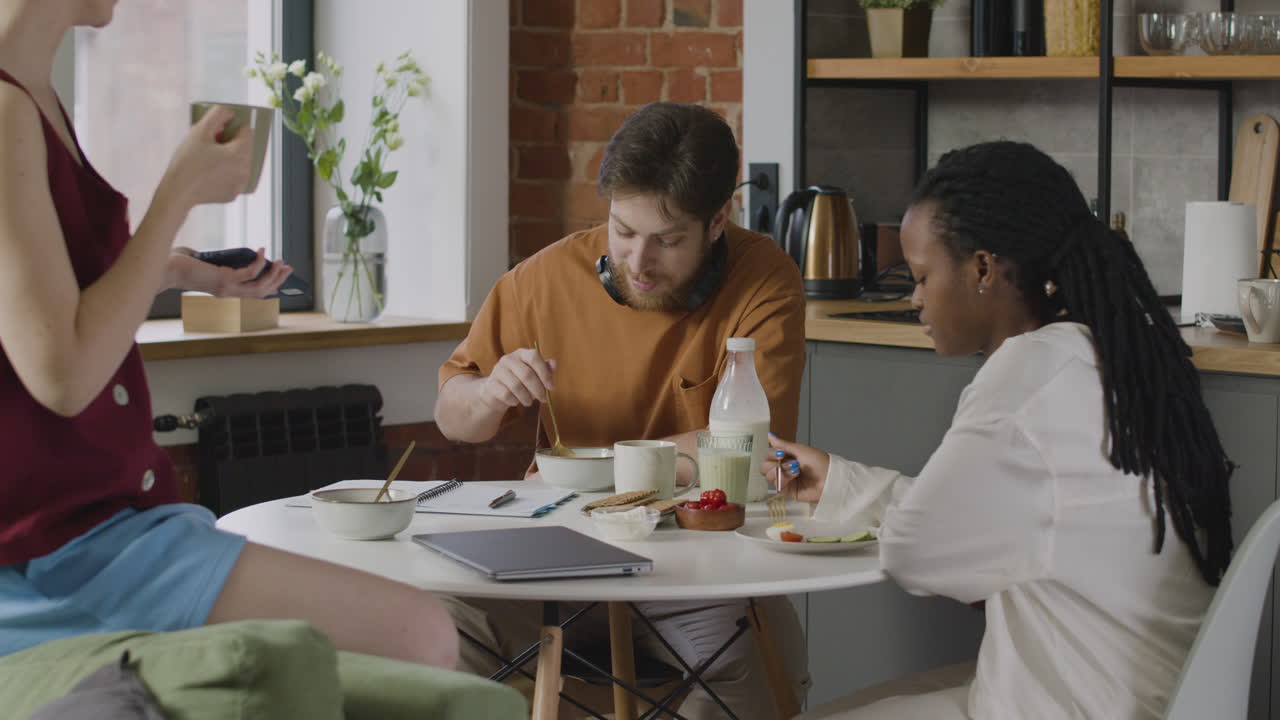 tres compañeros de cuarto desayunando y hablando juntos en la cocina 1