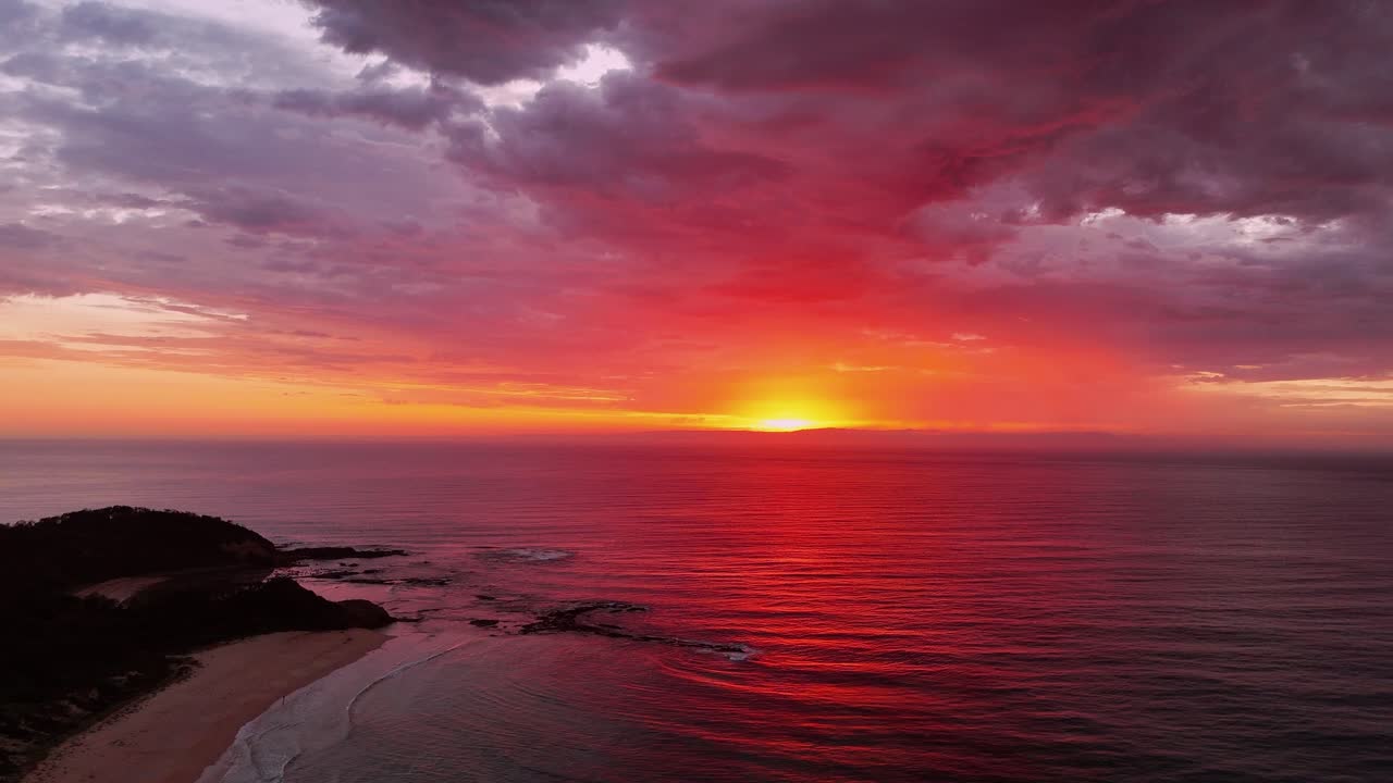 Stunning aerial pullback of a sunrise over Inyadda Beach, NSW, Australia, with glowing clouds above