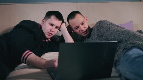 two men watching a laptop on a bed