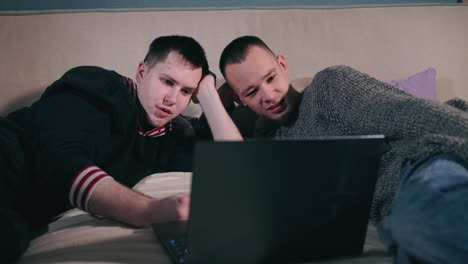 Two men watching a laptop on a bed