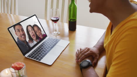 sección media de un hombre afroamericano con vino mientras hace una videollamada en una computadora portátil en casa
