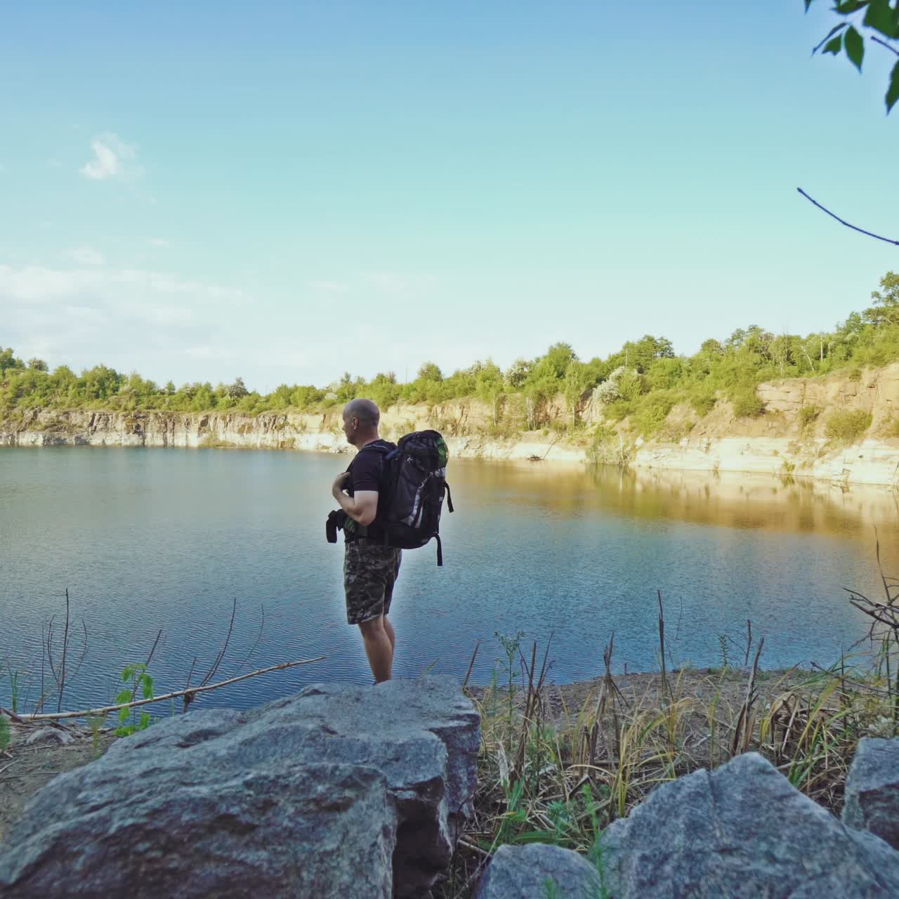 tourist with a backpack on his shoulders is looking at the colorful terrain by the river and walking along rock on the bank